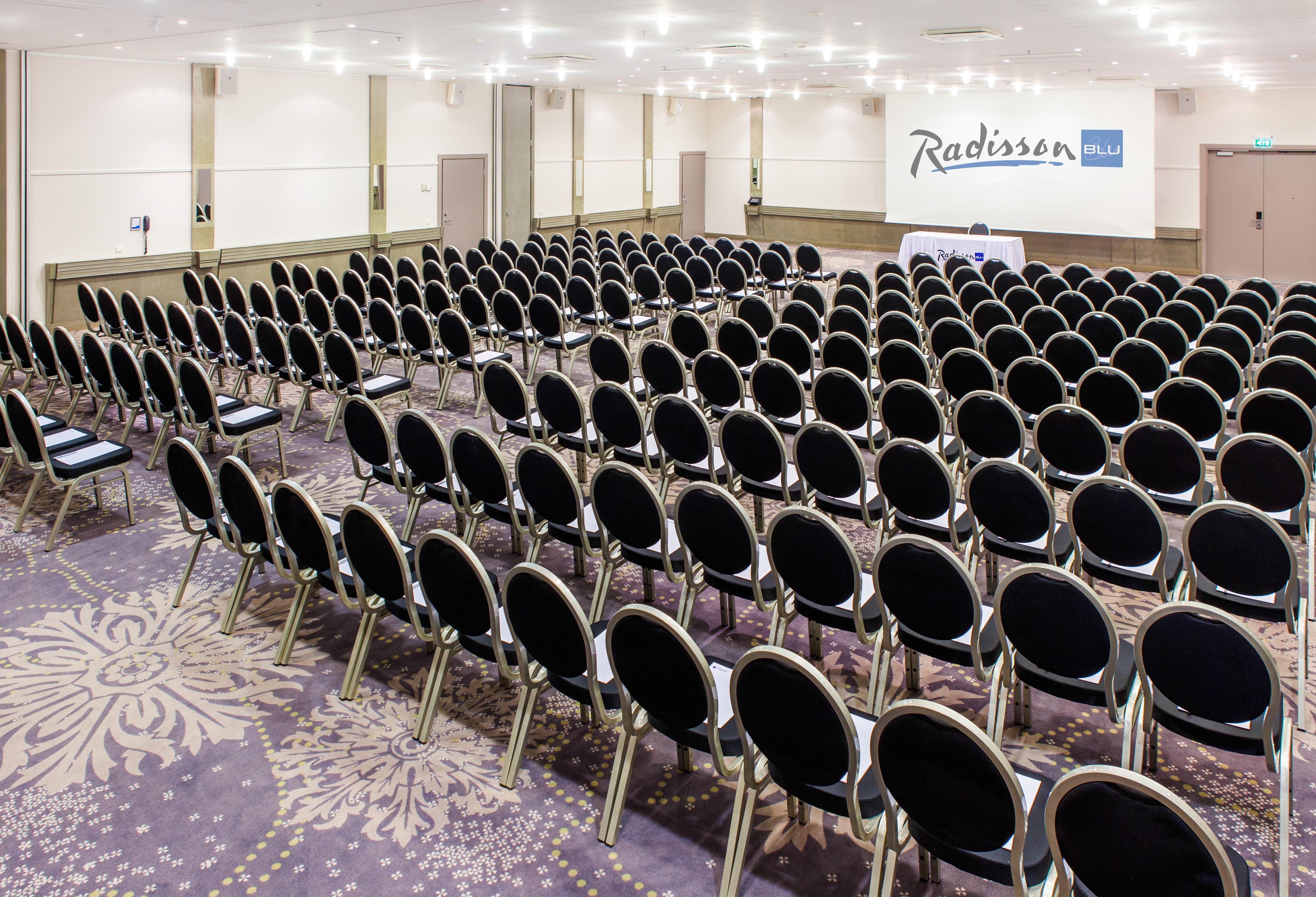Radisson Collection Hotel, Reval Exterior foto The photo shows a large conference room setup with rows of black chairs arranged facing a stage or presentation area at the front. The room has a light-colored carpet with a decorative pattern and is well-lit, featuring ceiling lights. In the backgro